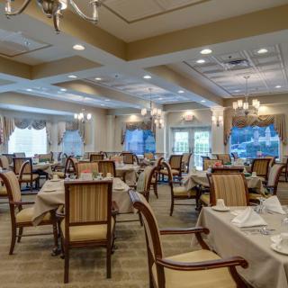 An elegant dining room with neatly arranged tables and chairs, featuring chandeliers and decorative elements.