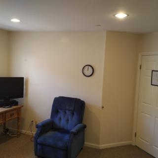 A cozy living room with a blue armchair, television, and wall clock.