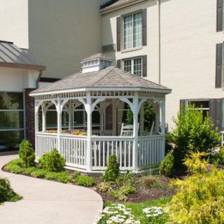 A charming white gazebo surrounded by lush greenery and a well-maintained garden, situated next to a building.
