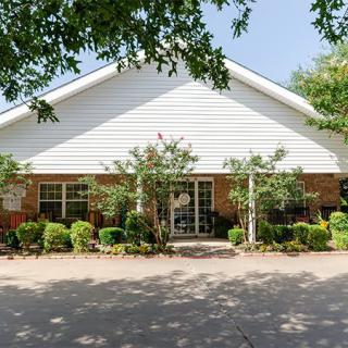 A well-maintained residential building with a front yard featuring trees and shrubs under a sunny sky.