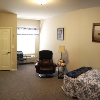 A cozy bedroom with an armchair, bed, and lamp near a window.