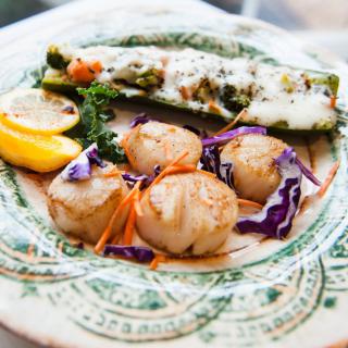 A gourmet plate featuring seared scallops, stuffed zucchini, and lemon garnish.