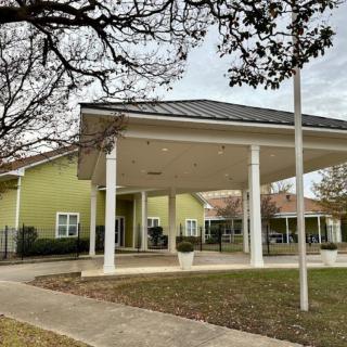 A building with a wide entrance supported by columns, surrounded by trees and grass under an overcast sky.