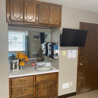 A cozy kitchen corner featuring a sink, wooden cabinets, a mirror, and a television.