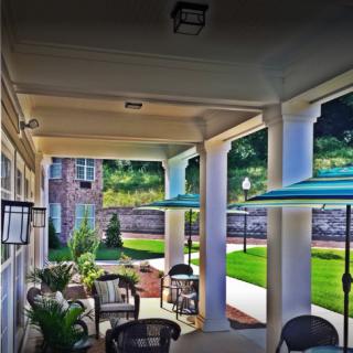 A shaded patio with outdoor furniture and columns overlooking a landscaped garden.