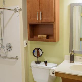 Modern bathroom with a shower, toilet, sink, and wooden cabinet.