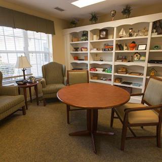 A cozy living room with comfortable chairs, a round table, and a bookshelf filled with various items.