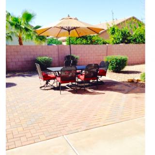 A sunny backyard patio with a dining set and umbrella on brick flooring.