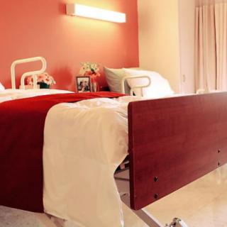 A clean and bright hospital room featuring a neatly made patient bed with a red accent wall.