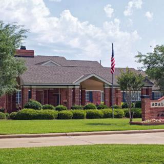 A brick residential building with a well-maintained lawn and an American flag displayed outside.