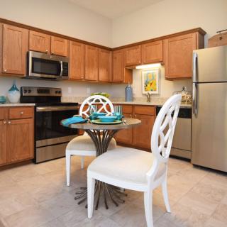 A modern kitchen with wooden cabinets, stainless steel appliances, and a small dining area.