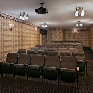 An empty home theater with rows of seating and a ceiling-mounted projector.