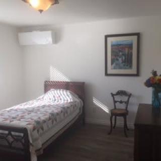 A minimalist bedroom with a single bed, a chair, and a framed painting on the wall.