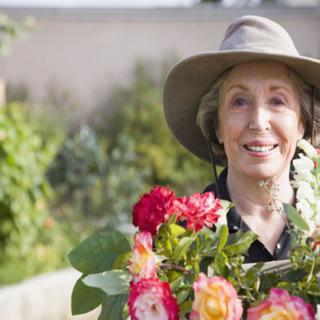 A senior woman smiling while holding a bouquet of flowers in a garden.