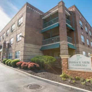 A brick apartment building with well-maintained landscaping and a sign at the entrance.