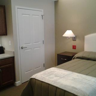 A cozy bedroom with a neatly made bed, wall-mounted lamp, and a closed door.