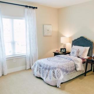 A cozy bedroom with a neatly made single bed beside a window, complemented by curtains and a nightstand with a lamp.