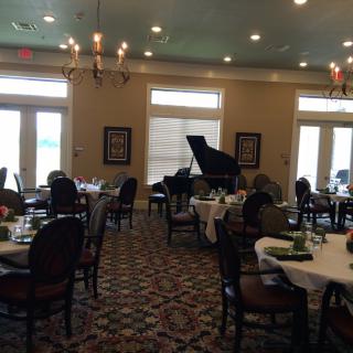 A dining room with round tables, a grand piano, and elegant chandeliers.