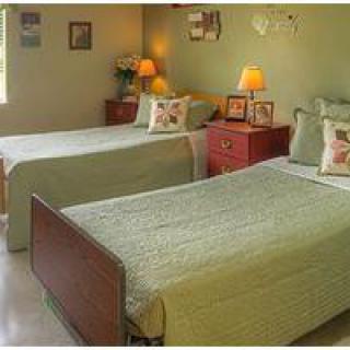 A cozy bedroom with two twin beds, decorated in soft green tones with matching pillows and bedside lamps.