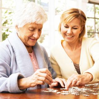 A middle-aged woman and an elderly woman working on a puzzle together at a table.