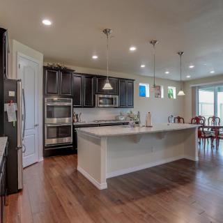 A modern kitchen with an island and pendant lighting, featuring dark cabinetry and hardwood floors.