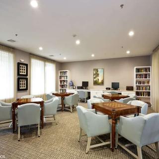 A well-lit meeting room with multiple tables and chairs, featuring bookshelves and computer stations.