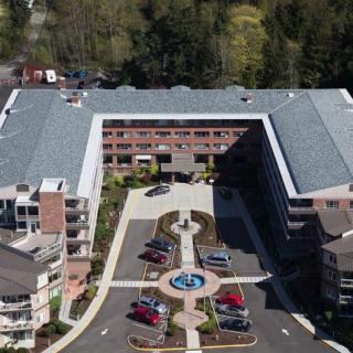 Aerial view of a large building with a central courtyard featuring a fountain and adjacent parking lot, surrounded by trees.