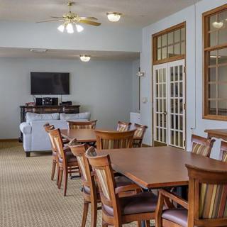 A communal dining area with multiple tables and chairs, a television, and a ceiling fan.