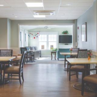 A modern dining area with tables and chairs, featuring a television and ample natural lighting.