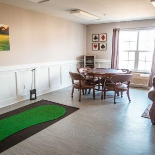 A cozy dining room with a round table and chairs, featuring a golf mat and wall art.