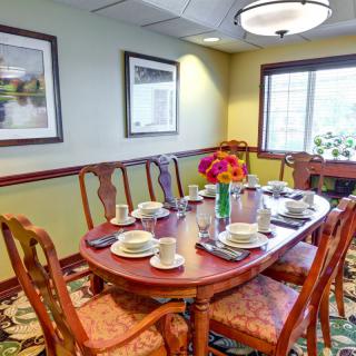 A cozy dining room with a table set for a meal, featuring elegant chairs, floral centerpiece, and framed artwork on the walls.