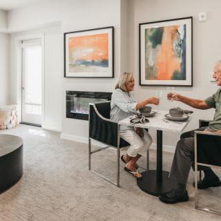 An elderly couple enjoys a meal in a modern, well-decorated living and dining area.