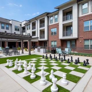 A modern apartment courtyard featuring a giant chess set on a lawn.