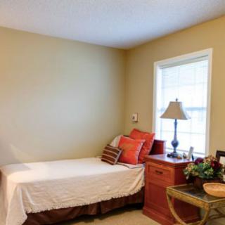 A cozy bedroom with a single bed, colorful pillows, and a wooden nightstand by the window.
