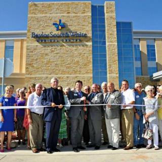 A group of people participates in a ribbon-cutting ceremony outside a large building.