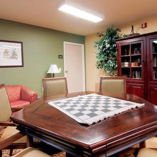 A well-furnished meeting room with a chessboard on the table, surrounded by chairs and bookshelves.