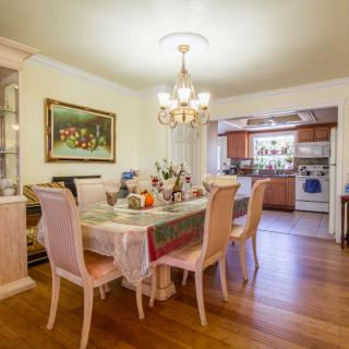 A dining area with a table set for a meal, featuring a chandelier and adjoining kitchen.