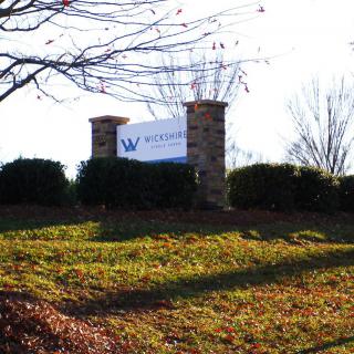 A sign on a grassy landscape with trees in the background.