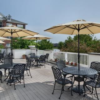 A spacious outdoor patio featuring tables and chairs with umbrellas, surrounded by greenery.