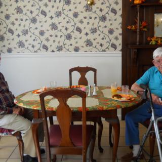 Two people sitting at a dining table in a room with floral wallpaper.