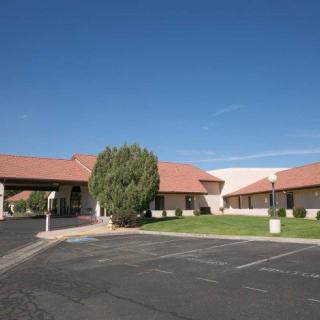 A single-story building with a red roof set against a clear blue sky, featuring a parking lot and landscaped area with a tree.