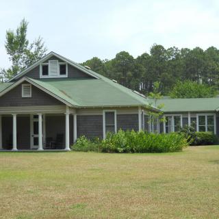 A rural house with a green roof, surrounded by a large lawn and trees.