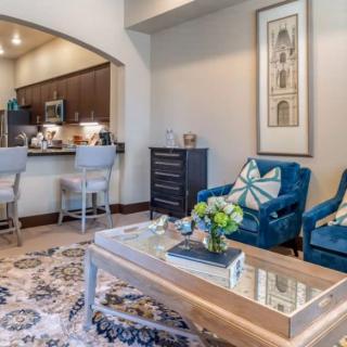 A modern living room with a cozy atmosphere, featuring blue chairs, a decorative coffee table, and an open view into the kitchen.