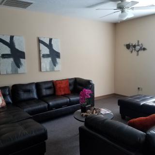 A modern living room with black leather sofas, abstract wall art, and a ceiling fan.