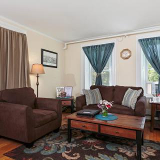 A cozy living room with a brown couch and armchair, a wooden coffee table, and colorful curtains.
