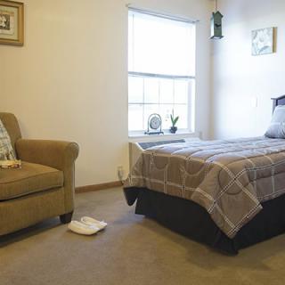A minimalist bedroom with a bed and armchair near a window.