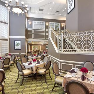 An elegant dining area with stylish tables and chairs, featuring a grand chandelier and decorative staircase.