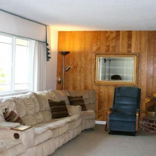 A cozy living room with a beige sofa, wood-paneled wall, and a large window.