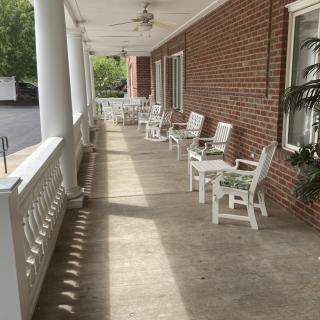 A long porch with white chairs and a brick wall, featuring a ceiling fan.