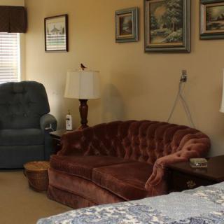 A cozy living room featuring a brown sofa, an armchair, and various paintings on the wall.